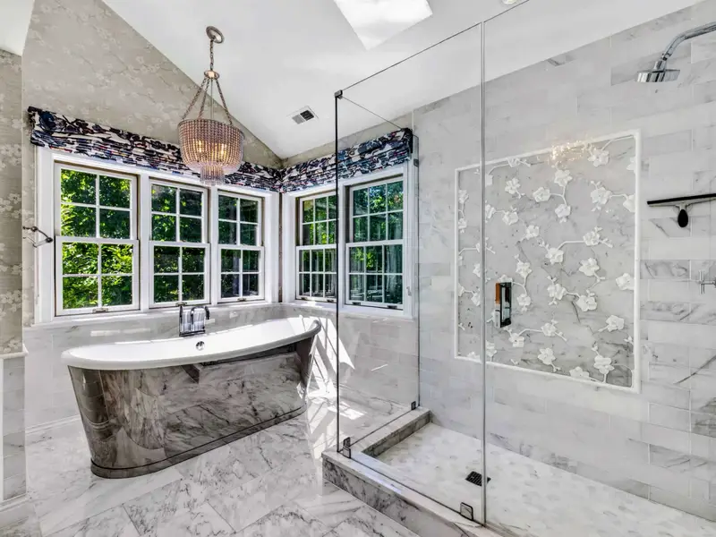Primary Bath - Detail of the shower with marble walls and herringbone floor tile.