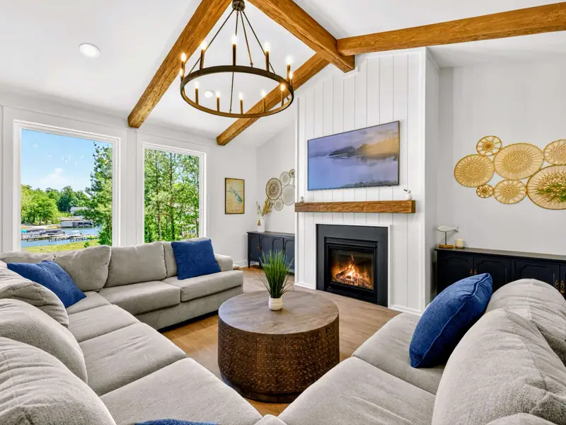 Great Room - A wraparound sectional faces the fireplace and Smart TV beneath vaulted wood beams, with lake and marina views out the windows.