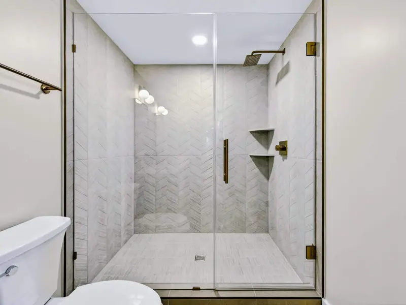 Walk-In Shower - Chevron-tiled walls and a gold rainhead finish the lower-level king suite's private walk-in shower.