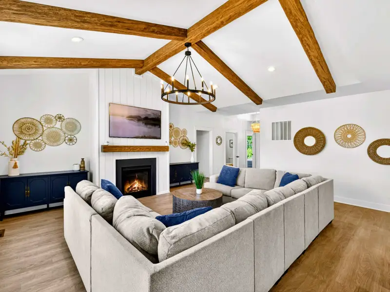 Great Room - An open layout wraps a sectional and sofa around the fireplace, vaulted beams overhead and the foyer and lake just beyond.