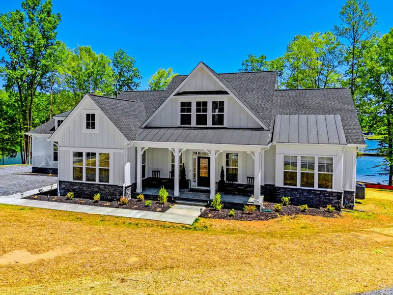 Exterior - The welcoming facade with rocking chairs on the covered porch, stone skirting, and glimpses of the lake to the right through the trees.