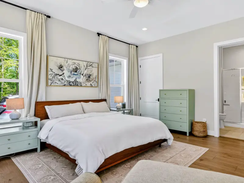 Bedroom 2 - Wood-framed king bed flanked by sage nightstands and a matching dresser, with an attached tiled glass-door shower just beyond.