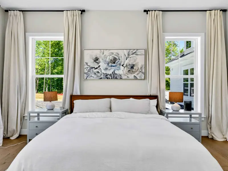Bedroom 2 - Symmetrical king setup with linen drapes pooling at both windows, paired nightstands, lamps, and soft natural light throughout.