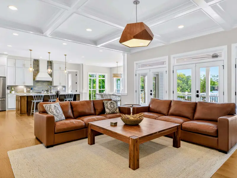 Great Room - Sunlight pours through French doors onto the leather sectional, with the white kitchen and island bar seating just steps away for effortless entertaining.