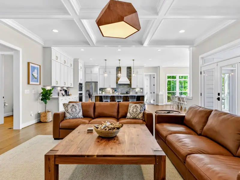 Great Room - Plush leather sofas and a faceted wood pendant set the tone, with sightlines straight through to the island and pendant-lit kitchen beyond.