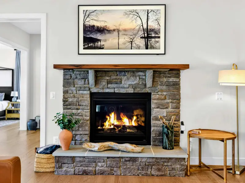 Great Room - Detailed view of the floor-to-mantel stacked-stone fireplace with live-edge wood beam, framed lake art, and a peek into an adjoining bedroom.