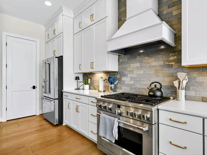 Chef's Kitchen - Pro stainless gas range with black kettle sits beneath a white hood and tile backsplash, flanked by white cabinetry and the fridge.