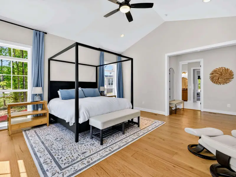 Primary Suite - The vaulted bedroom opens through wide doorway to a flex sitting area, with the canopy king bed glowing in morning light beside lake-facing windows.