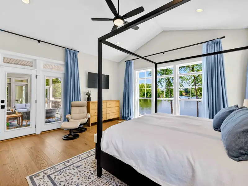 Primary Suite - French doors lead to the deck while a wall-mounted TV, oak dresser, and recliner share the airy room overlooking the calm cove just beyond.