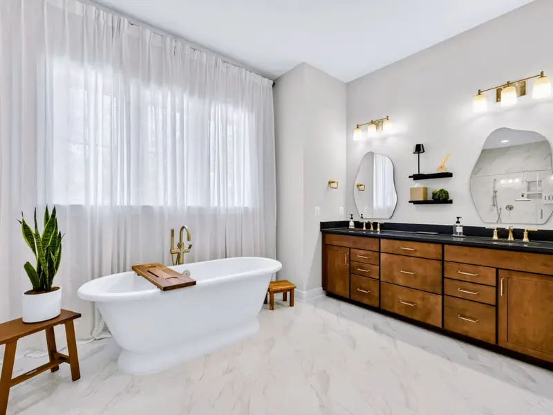 Primary Bath - The brass-fixtured soaking tub and rich wood double vanity pair beneath sculptural mirrors and warm sconce lighting for a true spa feel.