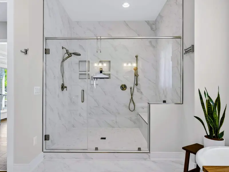Primary Bath - The oversized marble shower features dual heads, lit niches, a built-in bench, and a hand sprayer behind frameless glass for a luxe rinse.