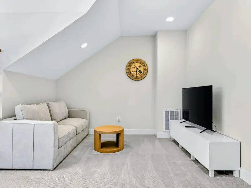 Loft - Cozy media corner featuring a soft sectional, round wood side table, wall-mounted flat screen, and a decorative lake-themed clock under sloped ceilings.