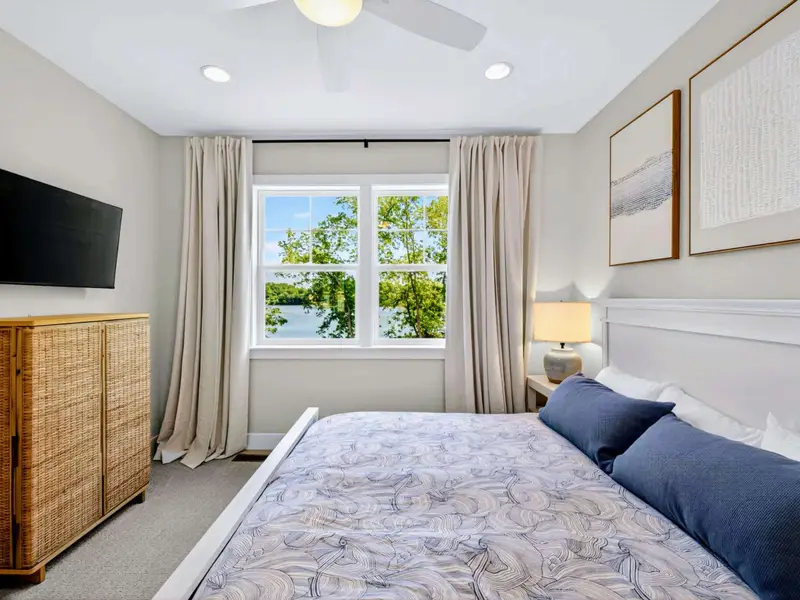 Bedroom 3 - King bed beside a window with a peaceful lake view, a woven dresser holding a mounted TV, and abstract framed art.
