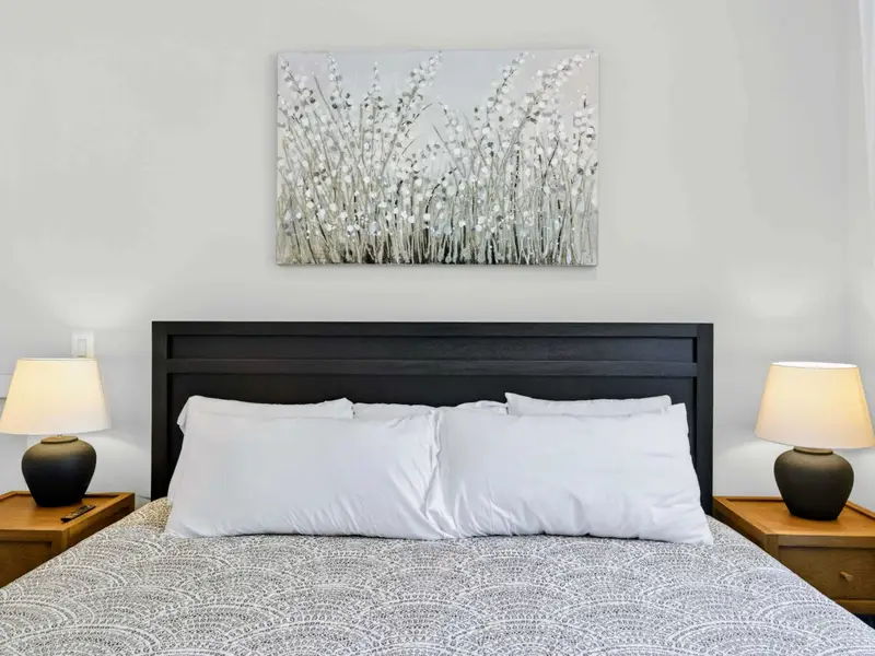 Bedroom 4 - Close headboard view of the king bed with crisp white pillows, twin black lamps on wood nightstands, and silvery floral art.