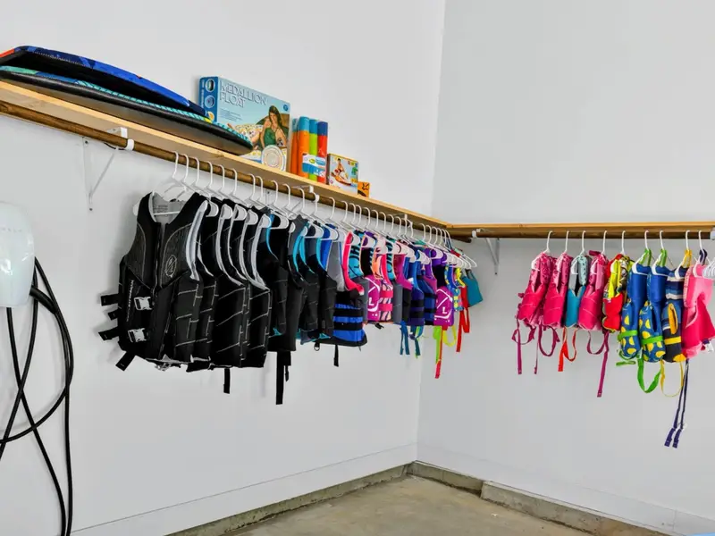Garage - A full lineup of life jackets in every size hangs ready on the wall, with floats and lake gear stocked on the shelf above.