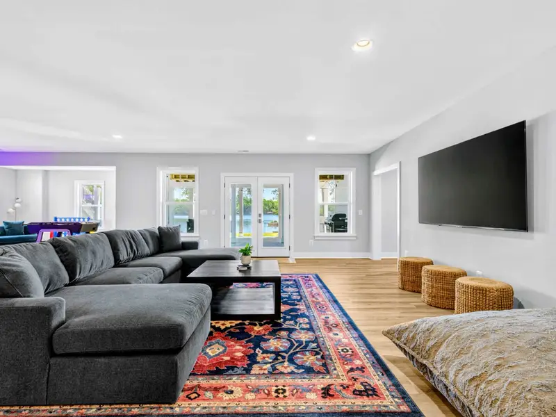 Game Room - Deep U-shaped sectional and bold patterned rug face a large flat screen, with arcade cabinets and a foosball corner visible across the space.