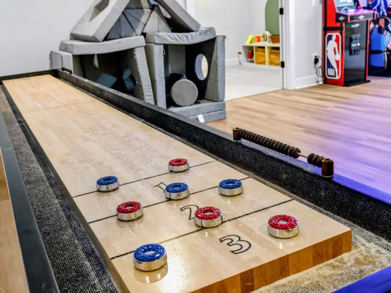 Game Room - Bright arcade corner with three classic cabinets under the GAME ON neon, a foosball table, blue swivel chair, and a giant Connect Four set.