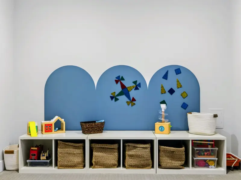 Kids' Playroom - Cheerful corner with a Making Waves banner, navy bean bag, canoe-shaped shelf, woven baskets, and a baby activity mat on soft carpet.