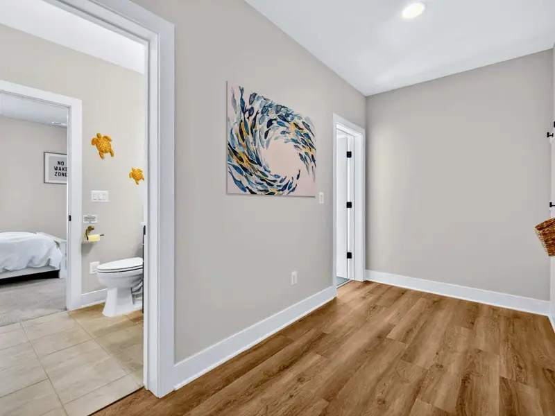 Lower-Level Hall - Wide-plank floors and framed art lead to the basement bedroom.