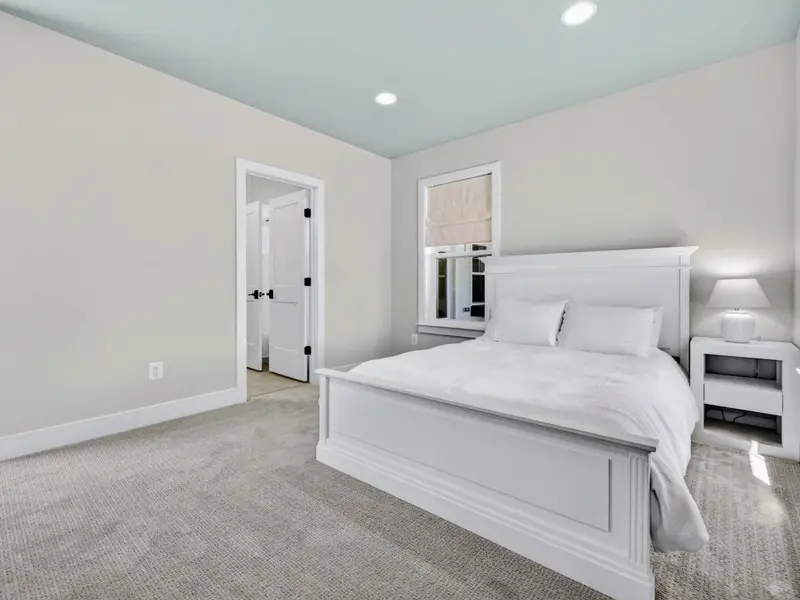 Bunk Suite - Crisp white queen bed with a tailored frame, nightstand and lamp, set against a calming pale-blue ceiling near an ensuite door.