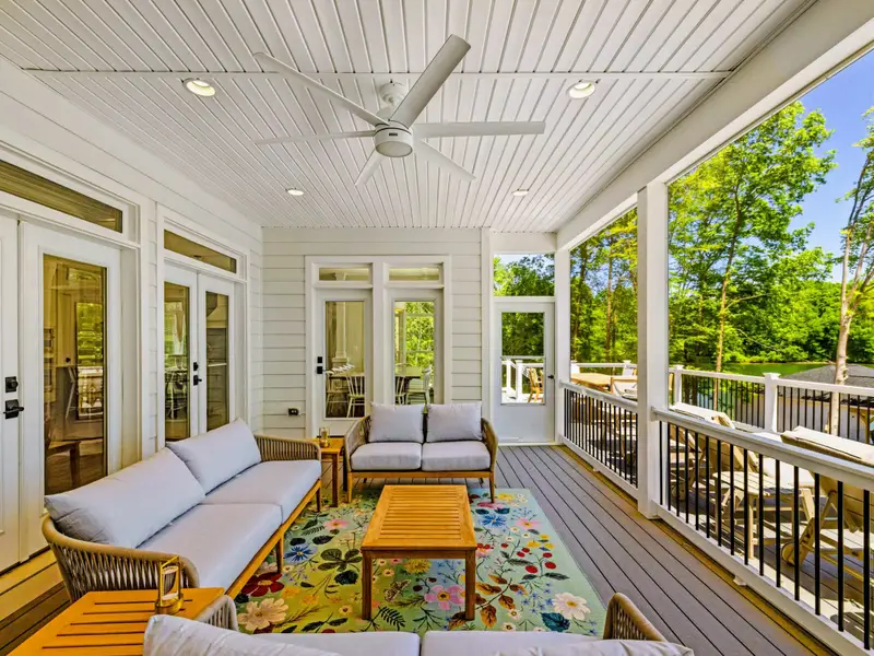 Screened Porch - Plush sofas and a wood coffee table on a floral rug invite easy lounging beside French doors and open treetop views.