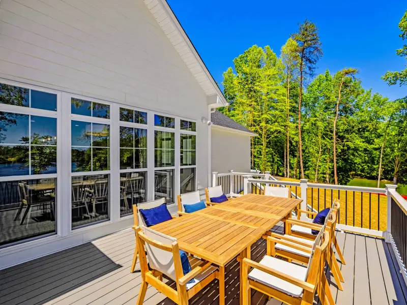 Deck - The teak dining table for six sits in full sun with a peek of the lake through the windows and open railing beyond.