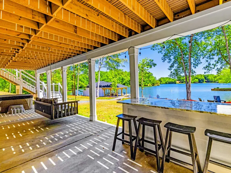 Covered Patio - Bar stools tuck under a granite counter overlooking the lake, with a hanging swing and hot tub area nearby.