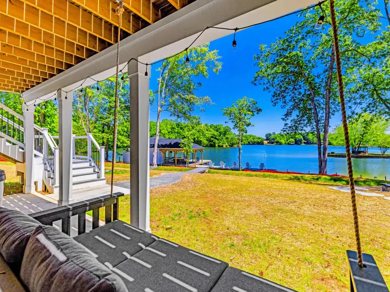 Covered Patio - A cushioned porch swing sways under string lights, looking out over the open lawn, dock, and tranquil water.