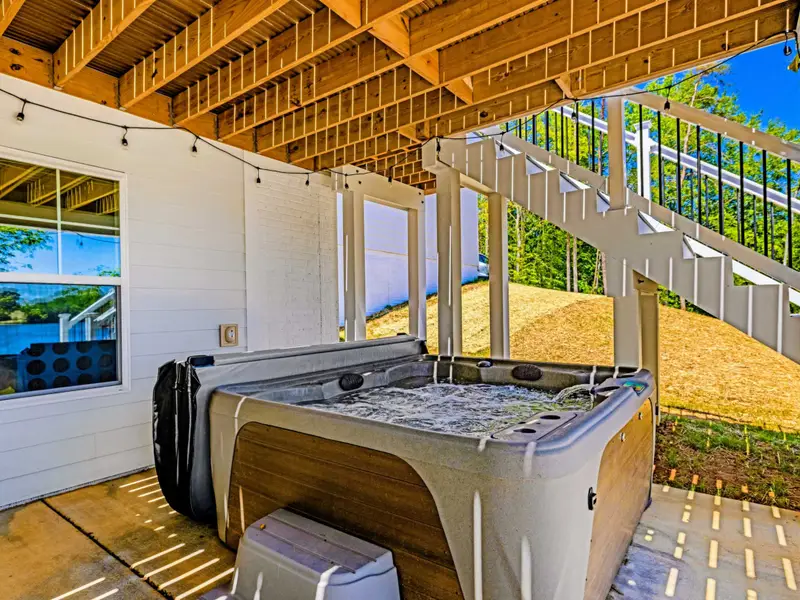 Covered Patio - A bubbling hot tub sits tucked beneath the stairs, ready for a soak with lake glimpses through the windows.