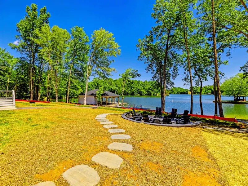 Fire Pit - A stepping-stone path winds across the lawn to the lakeside fire pit ringed with Adirondack chairs, water shimmering just beyond.