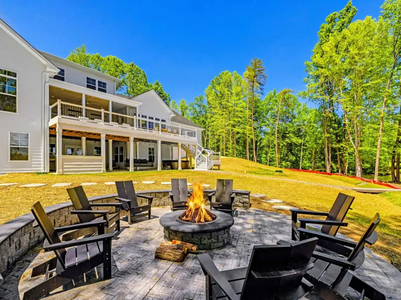 Fire Pit - Flames dance in the stone pit encircled by black Adirondack chairs, the stamped patio set against the home and wooded hillside.