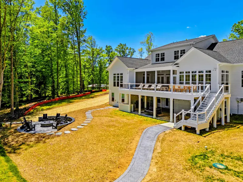 Backyard - Gentle green lawn sweeps from the home down toward the woods, with a covered screened porch, upper deck, and a stone fire pit ringed by chairs.
