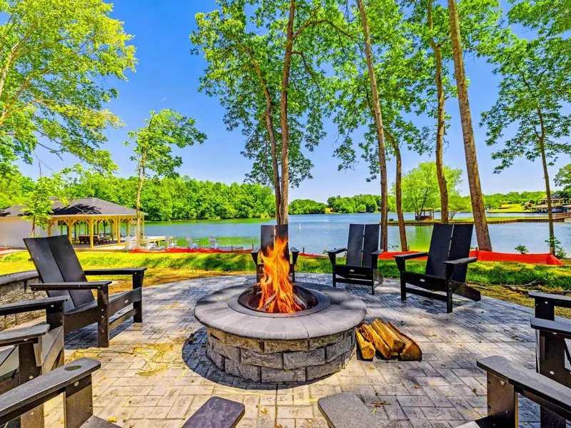 Fire Pit - Warm yourself by the lit fire pit and watch the sun catch the water, chairs arranged across the patio under shady trees.