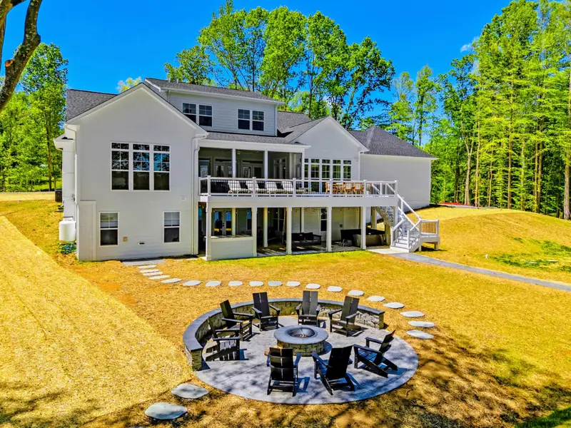 Fire Pit - The circular patio and fire pit sit just below the multi-level deck, surrounded by lawn and a backdrop of green woods.