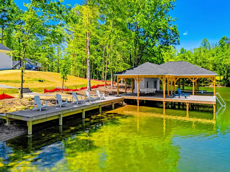Dock & Boathouse - A spacious dock with loungers leads out to the covered boathouse, the wooded shoreline reflected in the calm lake.
