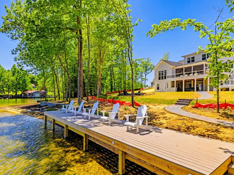 Dock & Boathouse - White Adirondack chairs cluster on the sunny dock with the home rising on the hillside behind and clear shallows below.