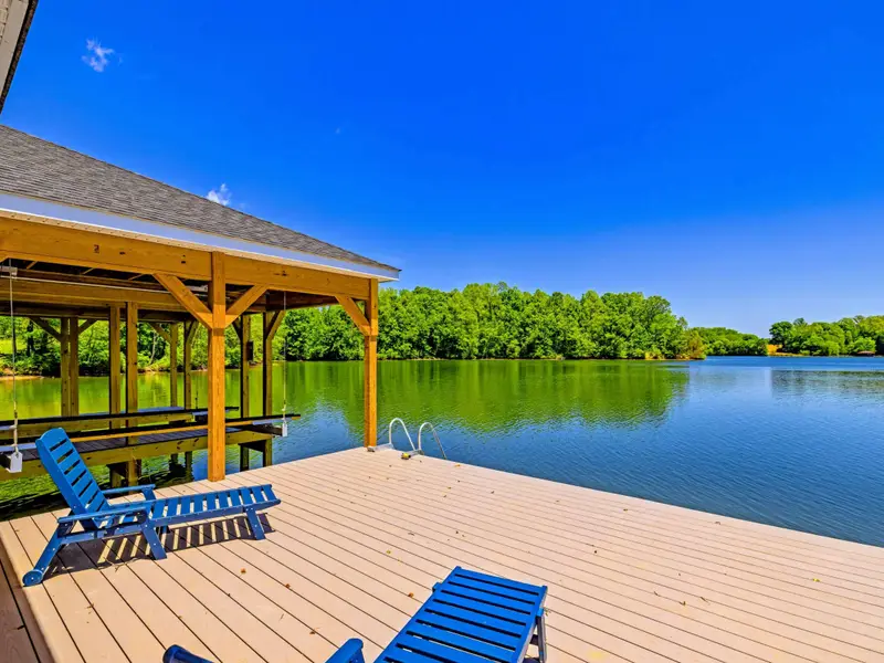 Dock & Boathouse - Blue chaise loungers line the sunny dock beside the covered pavilion, open water and green shoreline stretching ahead.