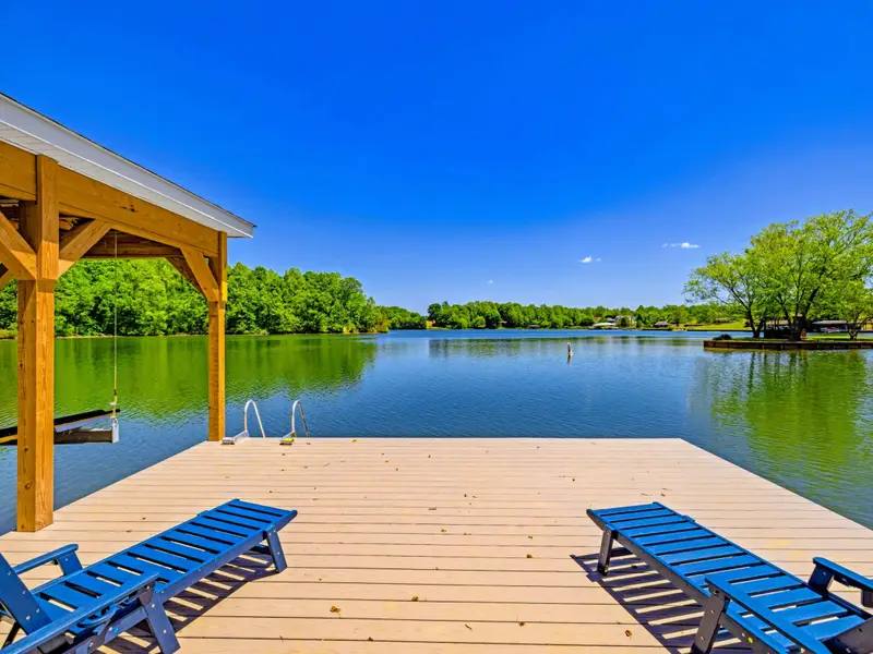 Dock & Boathouse - Blue loungers face an expansive lake view from the dock, the boathouse roofline shading one side over mirror-calm water.