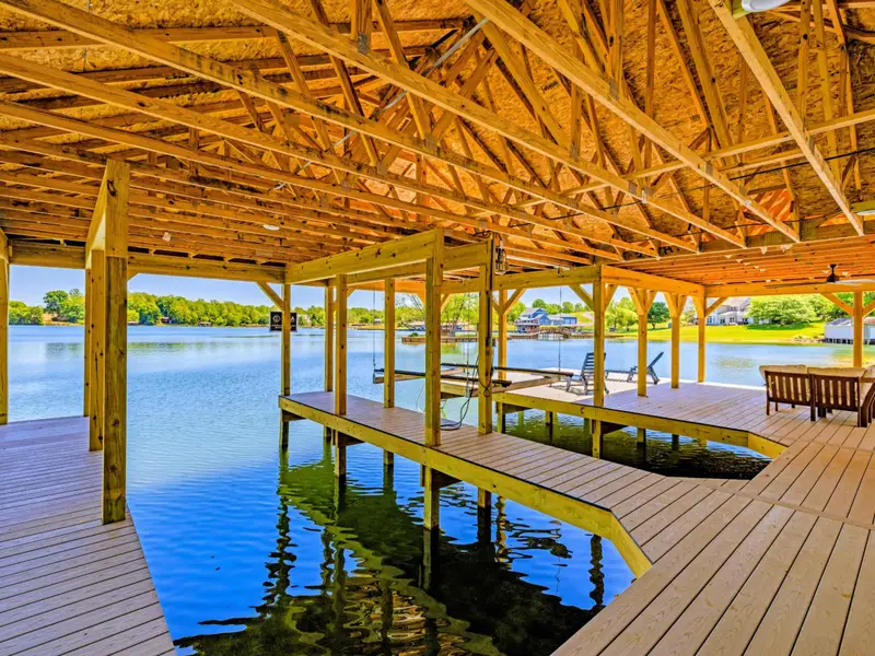 Dock & Boathouse - The double-slip covered boathouse frames the lake on both sides, a bench and loungers waiting on the sunlit dock.