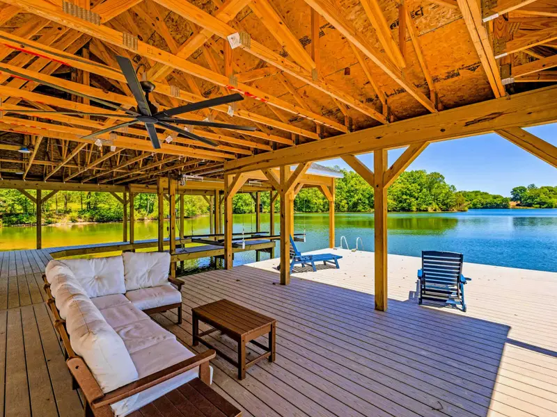 Dock & Boathouse - A cushioned sofa and coffee table create a shaded lounge under the boathouse roof, opening to chairs and water beyond.