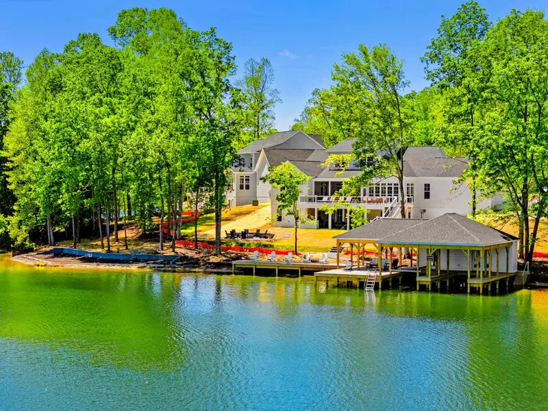 Dock & Boathouse - Aerial view of the grand home, terraced grounds, and covered boathouse meeting the emerald water amid lush trees.