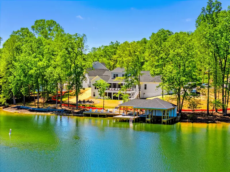 Aerial - Waterside view of the home nestled in the trees above a covered dock, its layered deck and porch overlooking the emerald-green cove.