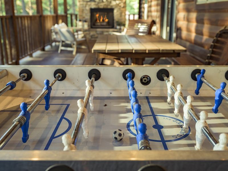 Foosball table with blue and white players, a small soccer ball, and a cozy cabin