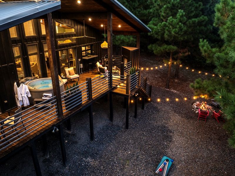 Modern cabin meets nature: hot tub, fire pit, and private deck surrounded by forest views and soft evening lights.