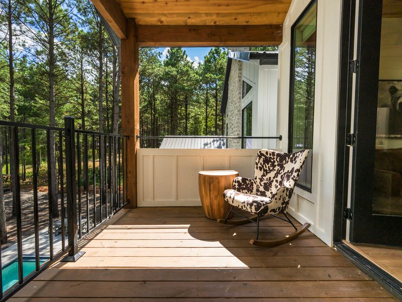 A sunny outdoor retreat features a cozy rocking chair and rustic wood accents overlooking the tranquil forest and pool below.