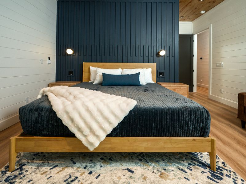 Beautifully styled king bedroom with rich green bedding and a custom wood accent wall.