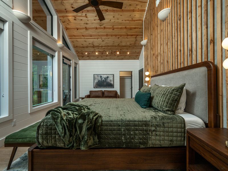Warm wood slats, glowing brass sconces, and layered green bedding create an inviting bedside retreat filled with rustic sophistication.