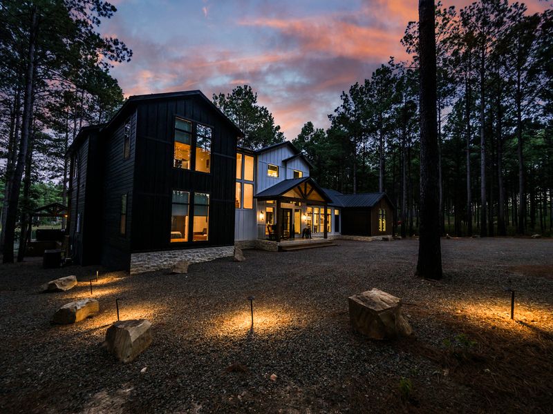 Modern lodge nestled among towering pines at dusk, showcasing large windows and inviting outdoor lighting