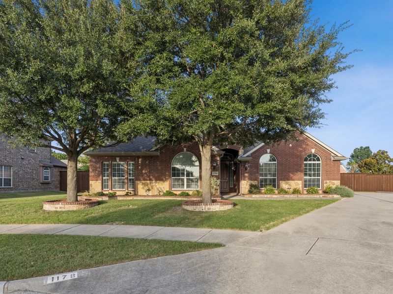 Beautifully landscaped front yard framed by mature shade trees.