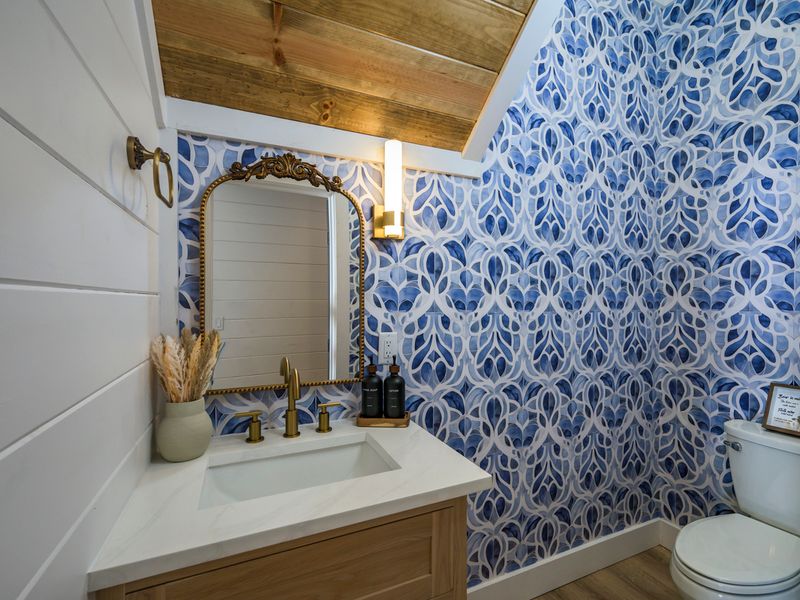 A bright and stylish bathroom featuring striking blue-and-white patterned walls, warm wood accents, and elegant gold fixtures.